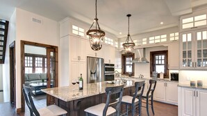 A spacious kitchen with a large island, white cabinetry, and hanging pendant lights.