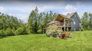 Une grande maison à deux étages dotée d’un balcon, entourée d’une pelouse bien entretenue et d’arbres.