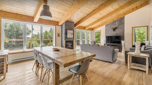 Un vaste espace de vie comprenant une table à manger en bois, des canapés gris et une cheminée.