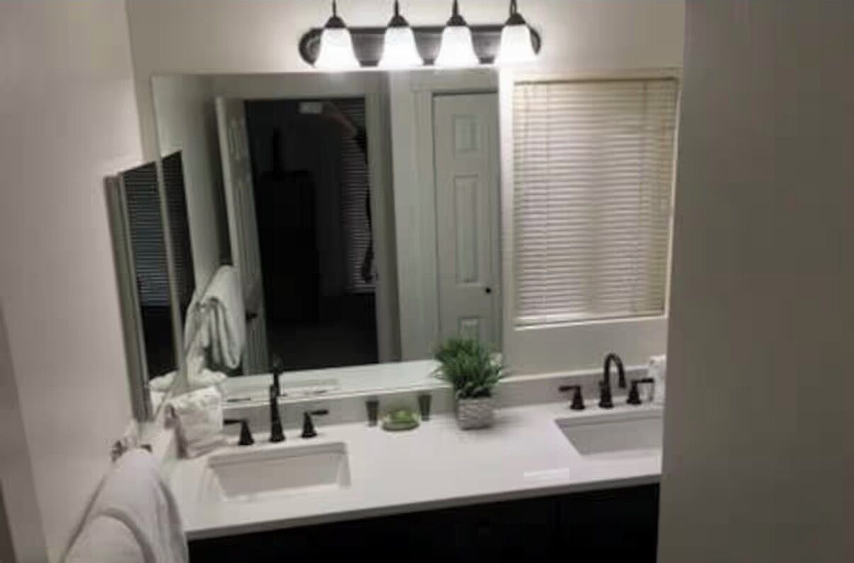Un baño con lavamanos blanco, espejo y planta en maceta.