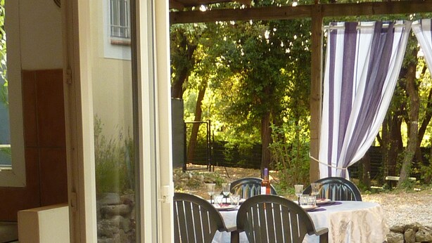 Een open terras met een tafel, stoelen, een barbecue en uitzicht op een tuin.