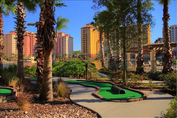 A miniature golf course with a winding path, surrounded by palm trees and greenery, with high-rise buildings in the background. - 2 Bedroom Resort Condo in Disney w/ Pools, Water Slides & Lazy Rivers (Lake Buena Vista)