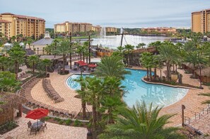 A resort with a large pool surrounded by palm trees and lounge chairs, a bridge over a body of water, and multiple hotel buildings in the background. - 2 Bedroom Resort Condo in Disney w/ Pools, Water Slides & Lazy Rivers (Lake Buena Vista)