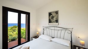 Relax in this serene bedroom with a large bed, framed artwork, and stunning garden and sea views.