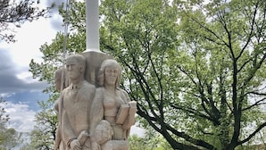 Un monument de pierre surmonté d’une plaque, installé dans un espace verdoyant, avec un mur de briques et des arbres en arrière-plan.