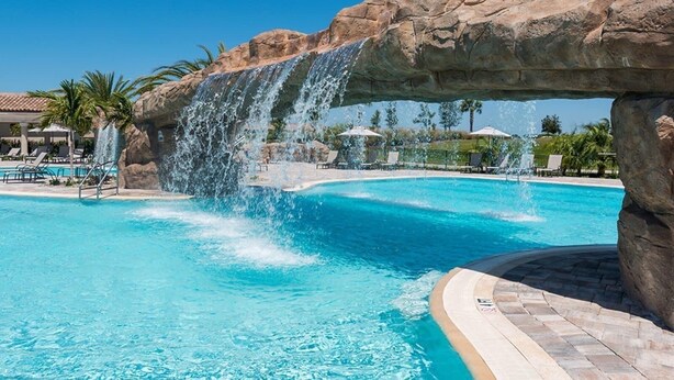 A pool with a waterfall feature, surrounded by lounge chairs and palm trees. - Lakewood National Golf and Resort,  3 Bed Condo -Unlimited Golf! (Lakewood Ranch)