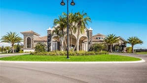 A residential building with a central arched entrance, surrounded by palm trees and a well-maintained lawn. - Lakewood National Golf and Resort,  3 Bed Condo -Unlimited Golf! (Lakewood Ranch)