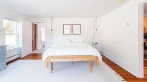 A bedroom with a large bed, a wooden bench, white walls, and a white door. - Renovated Catskills Farmhouse - hiking, swimming, quaint towns, 1st floor living (Denver)