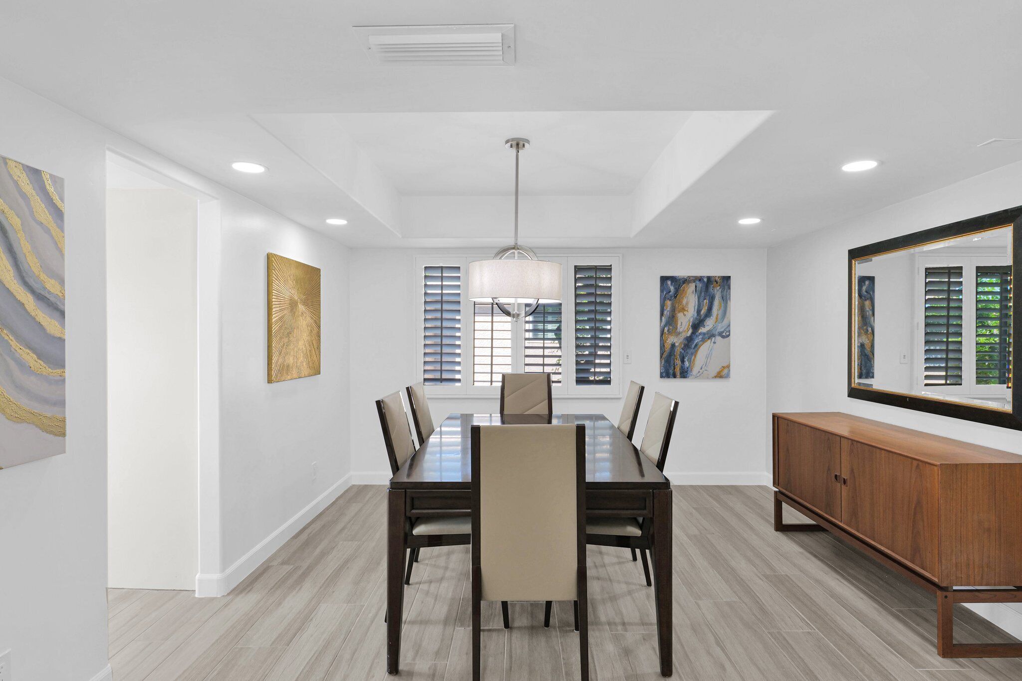 A dining room with a rectangular table, six chairs, a wooden cabinet, and artwork on the walls.