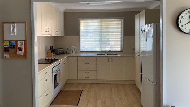 Eine kleine Küche mit weißen Schränken, einem Einbauofen, einem Kühlschrank und einem Fenster mit Jalousien.