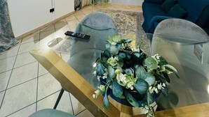 En moderne stue med et fladskærms-tv, en blå sofa, et glasbord og en blomsterdekoration.