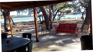 A covered outdoor seating area with a view of the beach and sea. - Cozy, private waterfront stone cabin on the north shore of Lake Travis (Lago Vista)