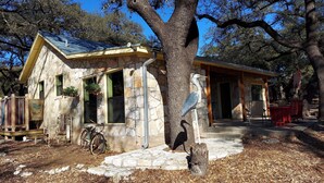 A rustic stone building with a metal roof, a bicycle, and a large tree in front. - Cozy, private waterfront stone cabin on the north shore of Lake Travis (Lago Vista)