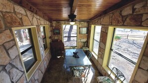 A stone-walled room with a table and chairs, large windows, and a ceiling fan. - Cozy, private waterfront stone cabin on the north shore of Lake Travis (Lago Vista)