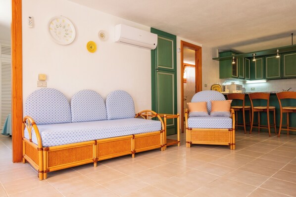 Una habitación con sofá, sillón, mesa de comedor y zona de cocina.