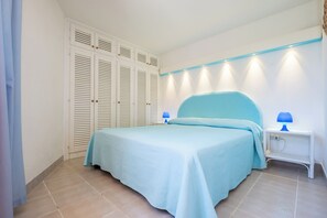 A bedroom with a bed, a nightstand, a lamp, a wardrobe, and a wall-mounted light fixture.