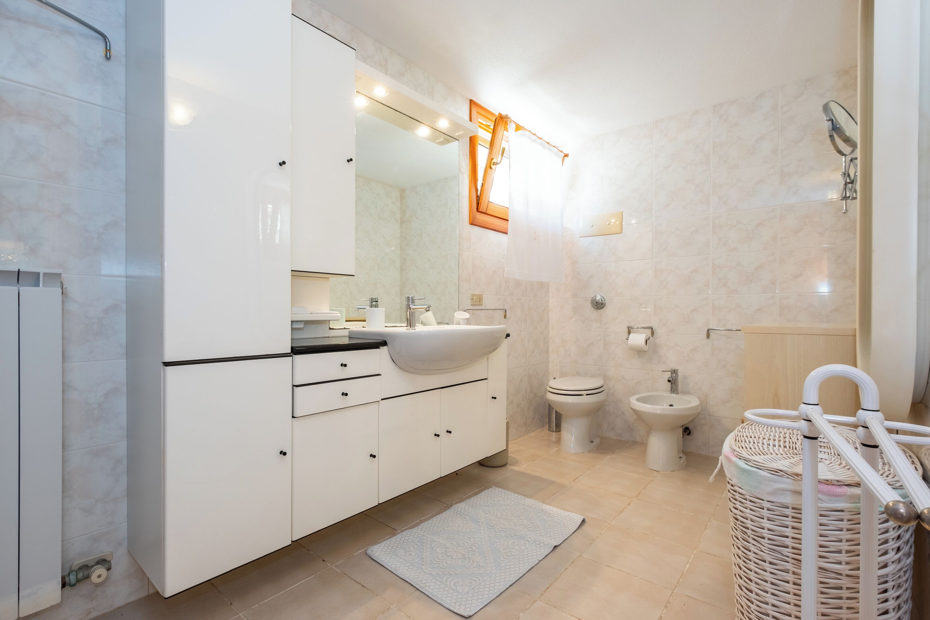 A modern bathroom with a white sink, mirror, and toilet, a small rug, and a wicker basket.