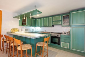A kitchen with green cabinets, a central island with stools, a microwave, and a stove.