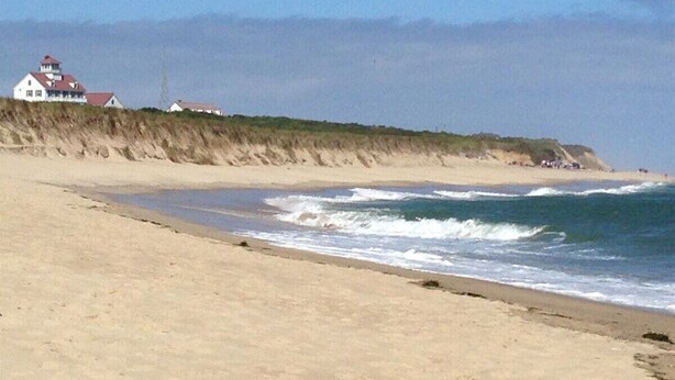 A beach with a white building with a red roof, a sandy shore, and waves crashing onto the beach. - Experience the charm of Cape Cod, a spacious 4-bedroom retreat in Eastham (Eastham)
