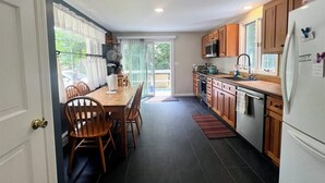 A compact kitchen with wooden cabinets, a white refrigerator, and a dining area with wooden chairs and a table. - Experience the charm of Cape Cod, a spacious 4-bedroom retreat in Eastham (Eastham)
