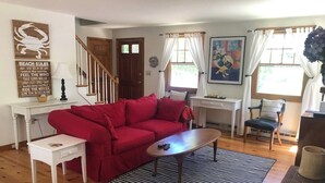 A living room with a red sofa, a coffee table, a striped rug, a blue patterned armchair, and a painting on the wall. - Experience the charm of Cape Cod, a spacious 4-bedroom retreat in Eastham (Eastham)