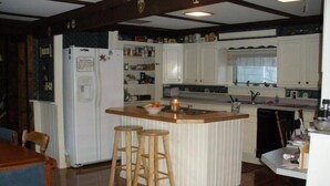 A kitchen with a central island, wooden stools, a refrigerator, and a sink. - Songo River Lodge: A retreat with access to Sebago Lake, Brandy Pond, Long Lake. (naples)