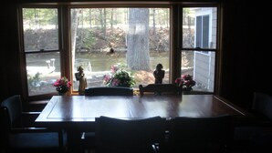 A dining area with a large window, a table, chairs, and a vase with flowers. - Songo River Lodge: A retreat with access to Sebago Lake, Brandy Pond, Long Lake. (naples)
