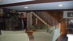 A living room with a stone fireplace, a wooden staircase, and a sofa. - Songo River Lodge: A retreat with access to Sebago Lake, Brandy Pond, Long Lake. (naples)