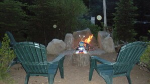 Two green Adirondack chairs facing a campfire with a sign that reads "Honey Maid." - Songo River Lodge: A retreat with access to Sebago Lake, Brandy Pond, Long Lake. (naples)