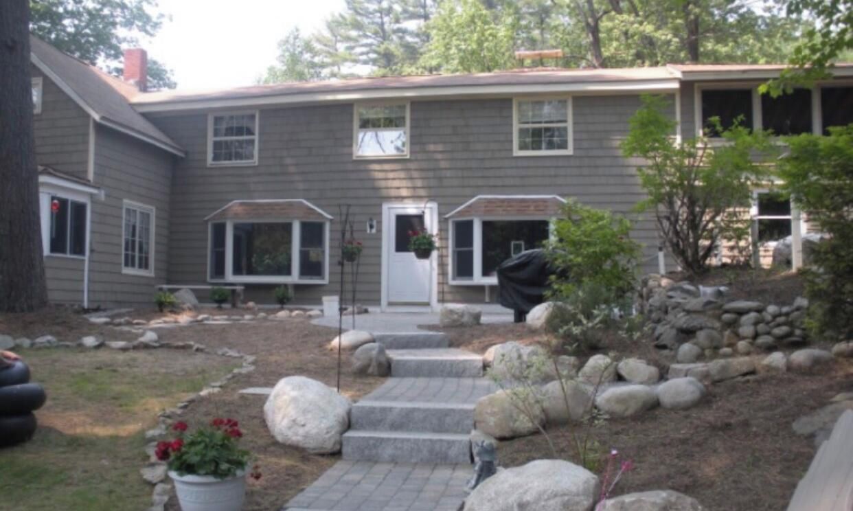 A two-story house with a front porch, a small garden with rocks and plants, and a covered outdoor seating area.