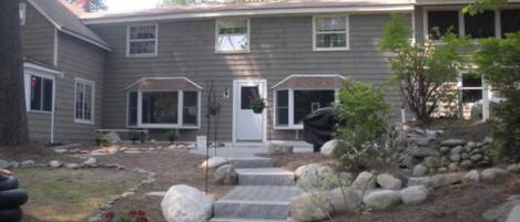 A two-story house with a front porch, a small garden with rocks and plants, and a covered outdoor seating area.