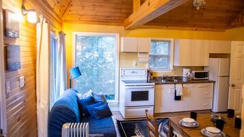 A compact kitchen with white appliances, a dining table with plates, and a blue sofa in a cabin-style room.