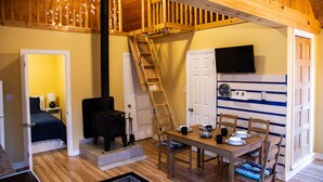 Une pièce chaleureuse avec un escalier en bois, une cheminée, une table à manger avec des chaises et un téléviseur fixé au mur.