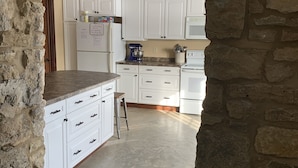A kitchen with white cabinets, a granite countertop, and a stone wall. - Hamilton Goebel House 816 E Louisa St Darlington Wi  (Darlington)
