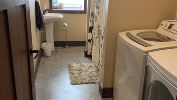 Ett litet badrum med ett handfat, en toalett, en duschdraperi och en tvättmaskin.