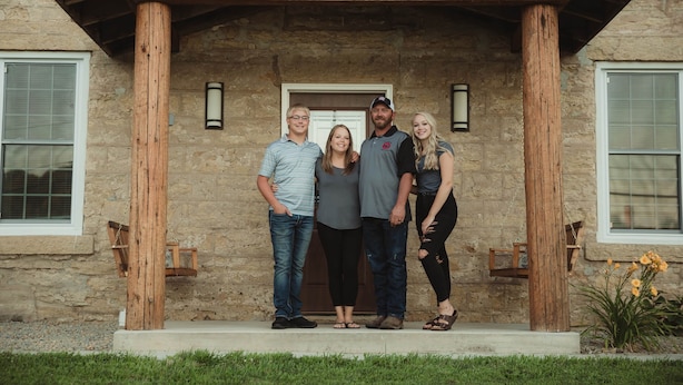 A family standing in front of a stone building with a wooden porch and a number '816' above the entrance. - Hamilton Goebel House 816 E Louisa St Darlington Wi  (Darlington)