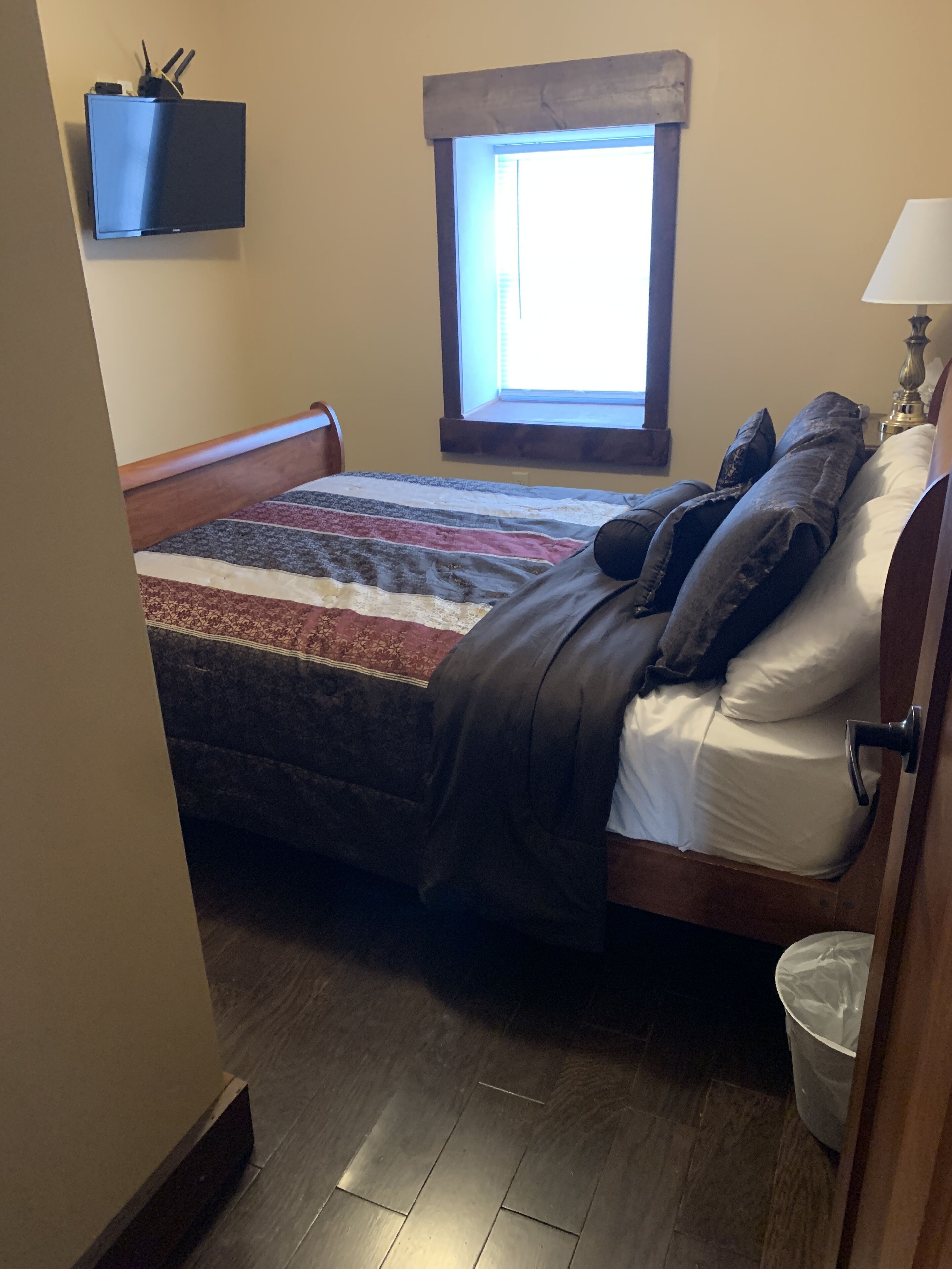 Une chambre à coucher avec un lit, une fenêtre, une lampe et une poubelle.