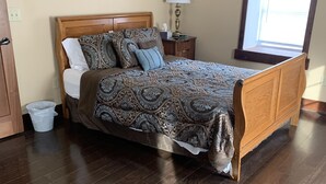 A bedroom with a wooden bed, a nightstand with a lamp, a window with blinds, and a wooden floor. - Hamilton Goebel House 816 E Louisa St Darlington Wi  (Darlington)