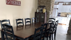 A dining area with a wooden table and chairs, a stone wall, and a kitchen in the background. - Hamilton Goebel House 816 E Louisa St Darlington Wi  (Darlington)