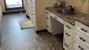 A bathroom with a sink, white cabinets, and a patterned shower curtain.