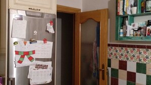 Una cocina con refrigerador, armarios de madera, salpicadero a cuadros y una puerta que da a otra habitación.
