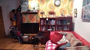 Una sala de estar acogedora con un sofá rojo, una estantería, una mesita con una lámpara y un reloj en la pared.