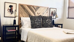 A neatly arranged bedroom with a bed, two nightstands, a patterned rug, and two framed artworks on the wall.