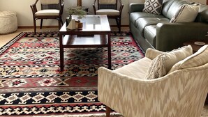A living room with a large window, two chairs, a sofa, a coffee table, and a patterned rug.