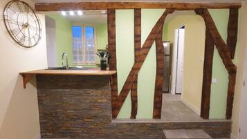 A kitchen with a stone countertop, a wooden beam structure, and a large clock on the wall.