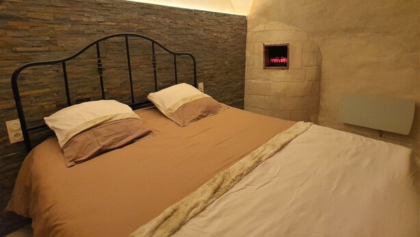 A bedroom with a stone wall, a metal headboard, and a small window with red lights.