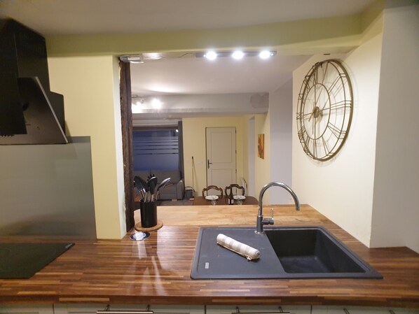 A kitchen with a wooden countertop, a sink, and a wall-mounted clock.