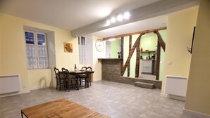 A spacious living area with a dining table, chairs, a fireplace, and a kitchen in the background.