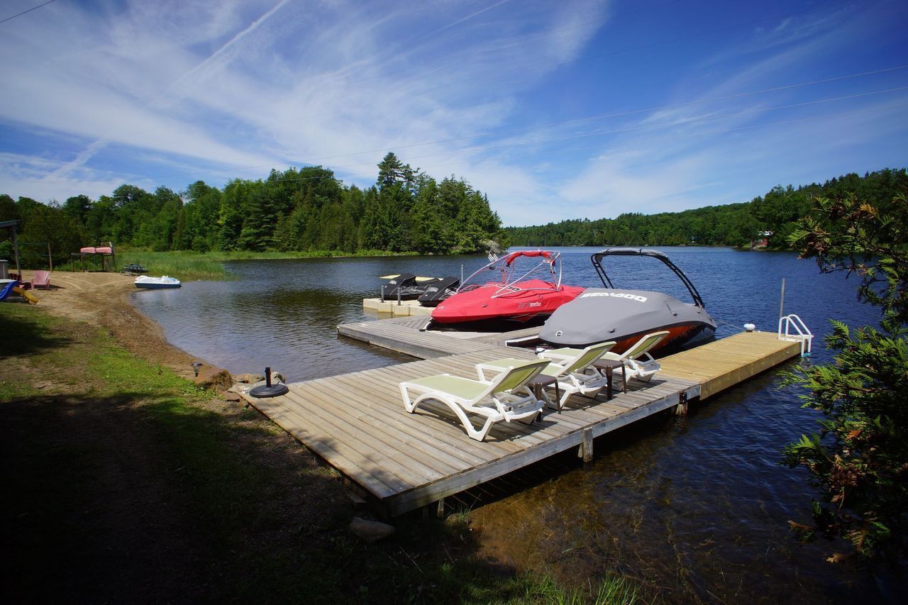 Un lago con un muelle, un jet ski rojo y dos sillas de descanso en el muelle.