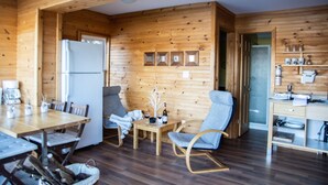 A wooden cabin interior with a dining table, chairs, a refrigerator, a small table with a bottle and glasses, and a wooden desk with shelves. - Lakeview Cottage - Myers Cave Resort (North Frontenac)
